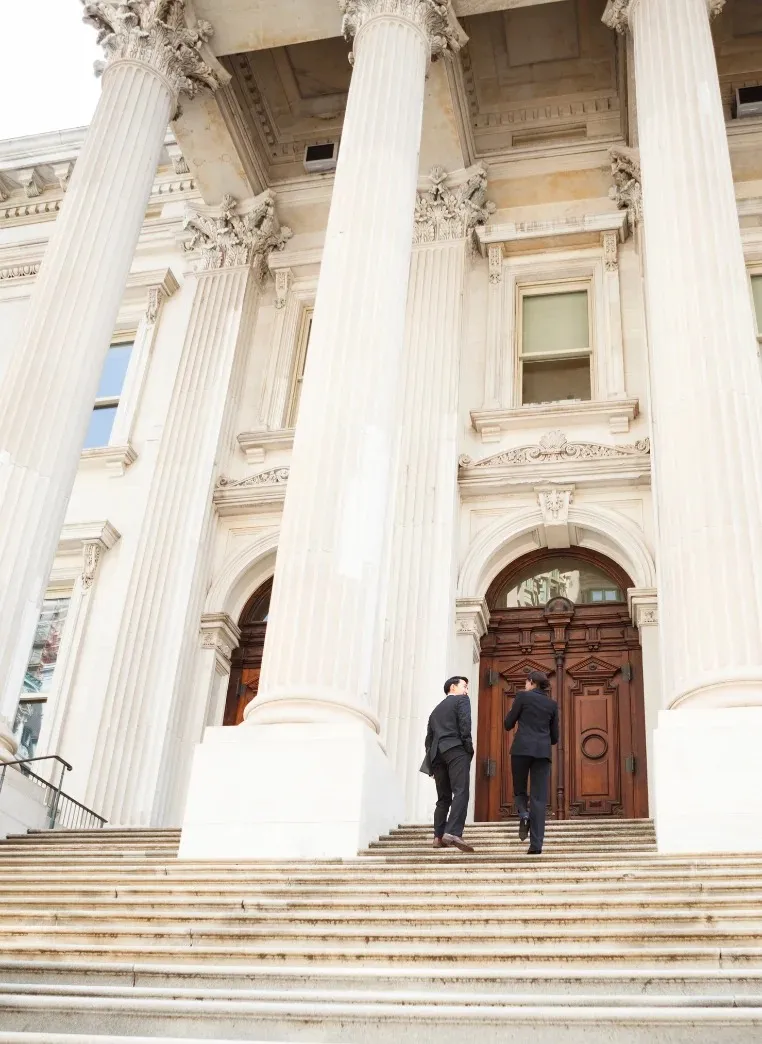 Two people in suits walking up the stone steps of a columned courthouse.