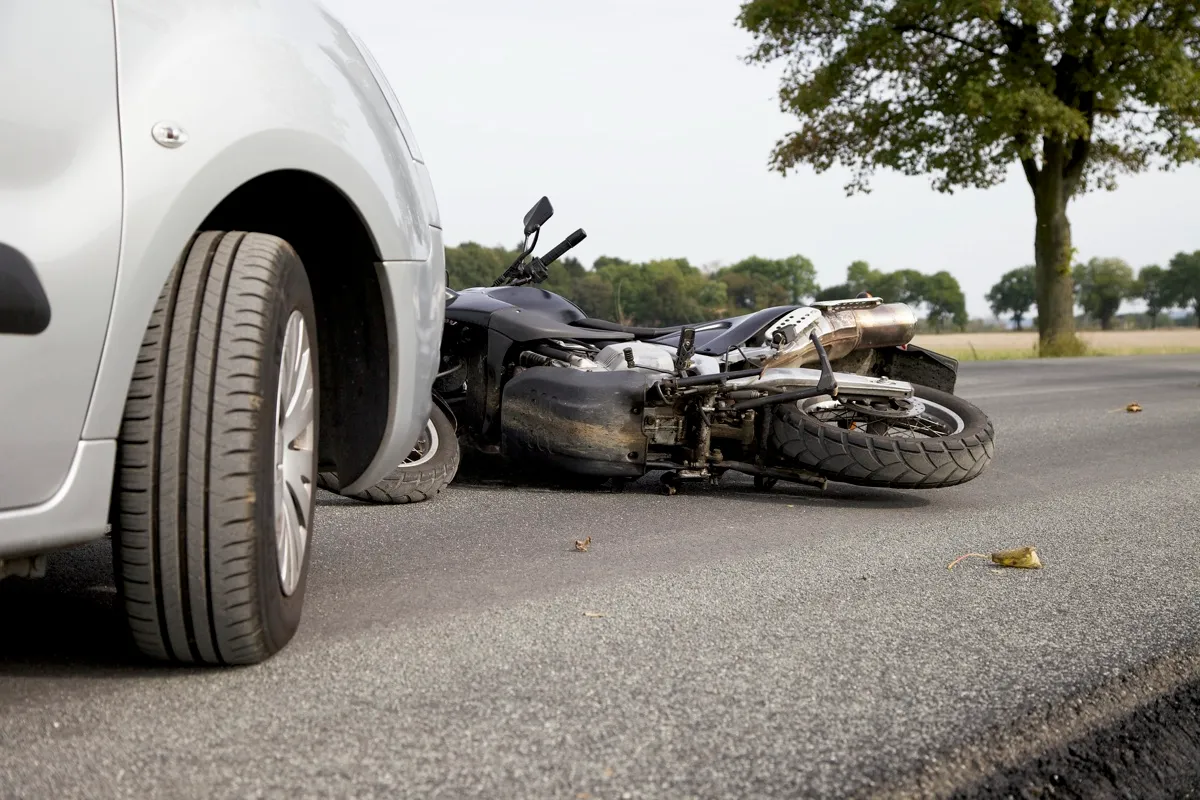 A motorcycle lying on its side on the road next to a car after a crash.